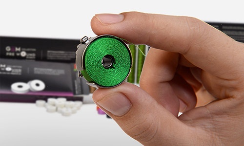 main tenant une bobine de fil prébobiné sans canette gem vert dans un boîtier de canette