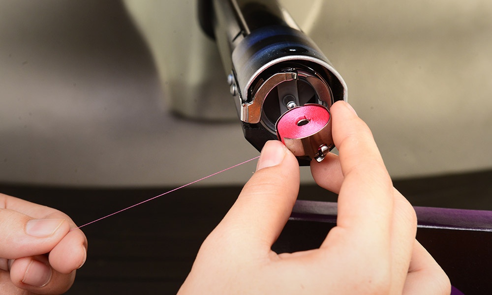 mão inserindo bobina pré-enrolada sem núcleo GEM na cor rosa na máquina de bordar