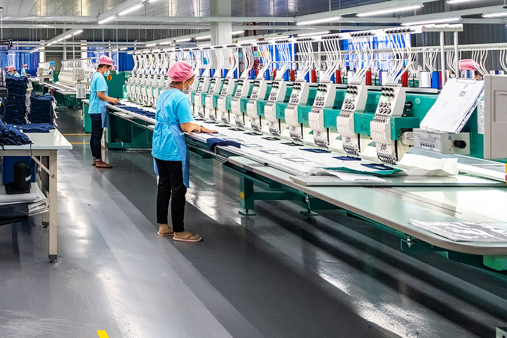 two factory workers operating embroidery machine